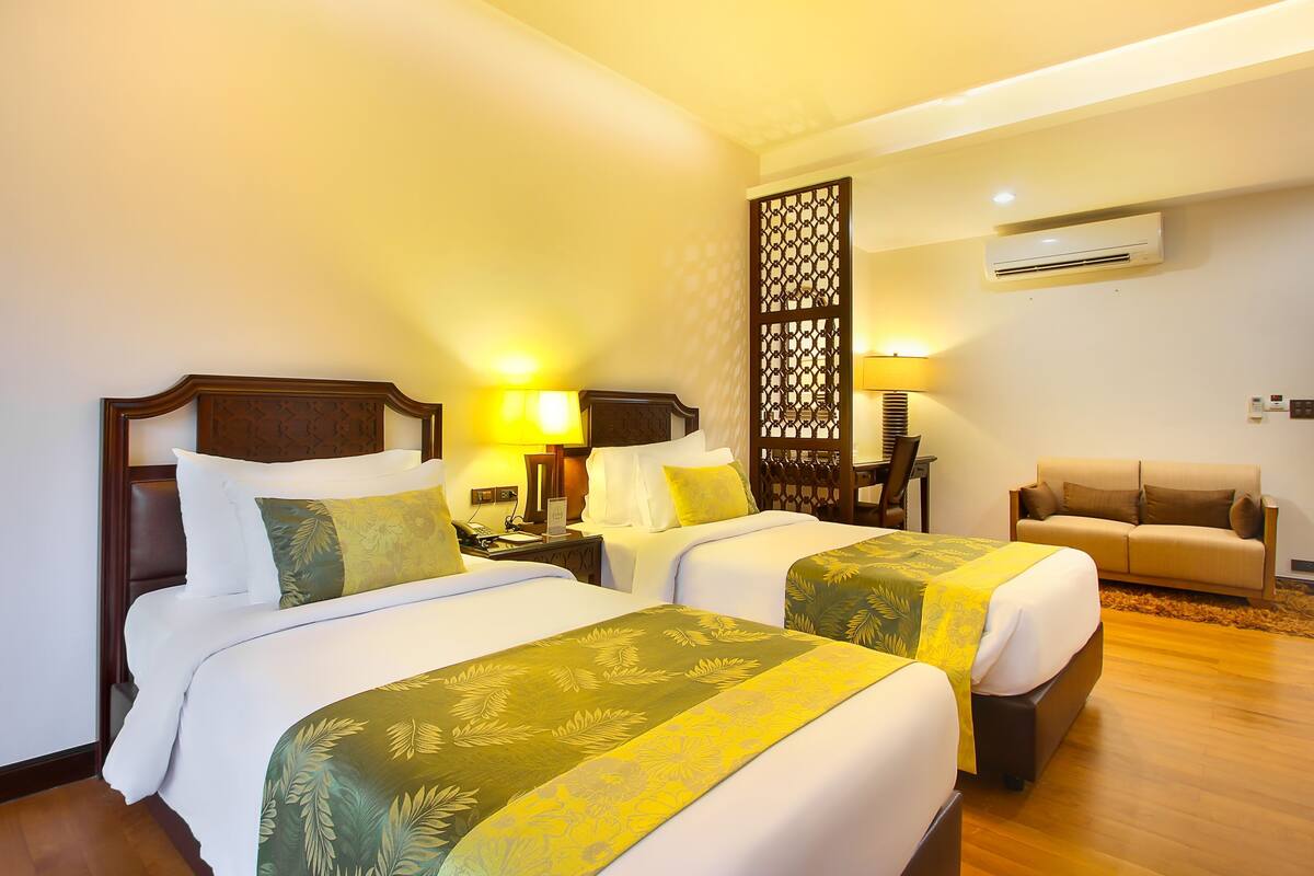 Una habitación de hotel con dos camas, un sofá, un separador decorativo y un equipo de aire acondicionado.