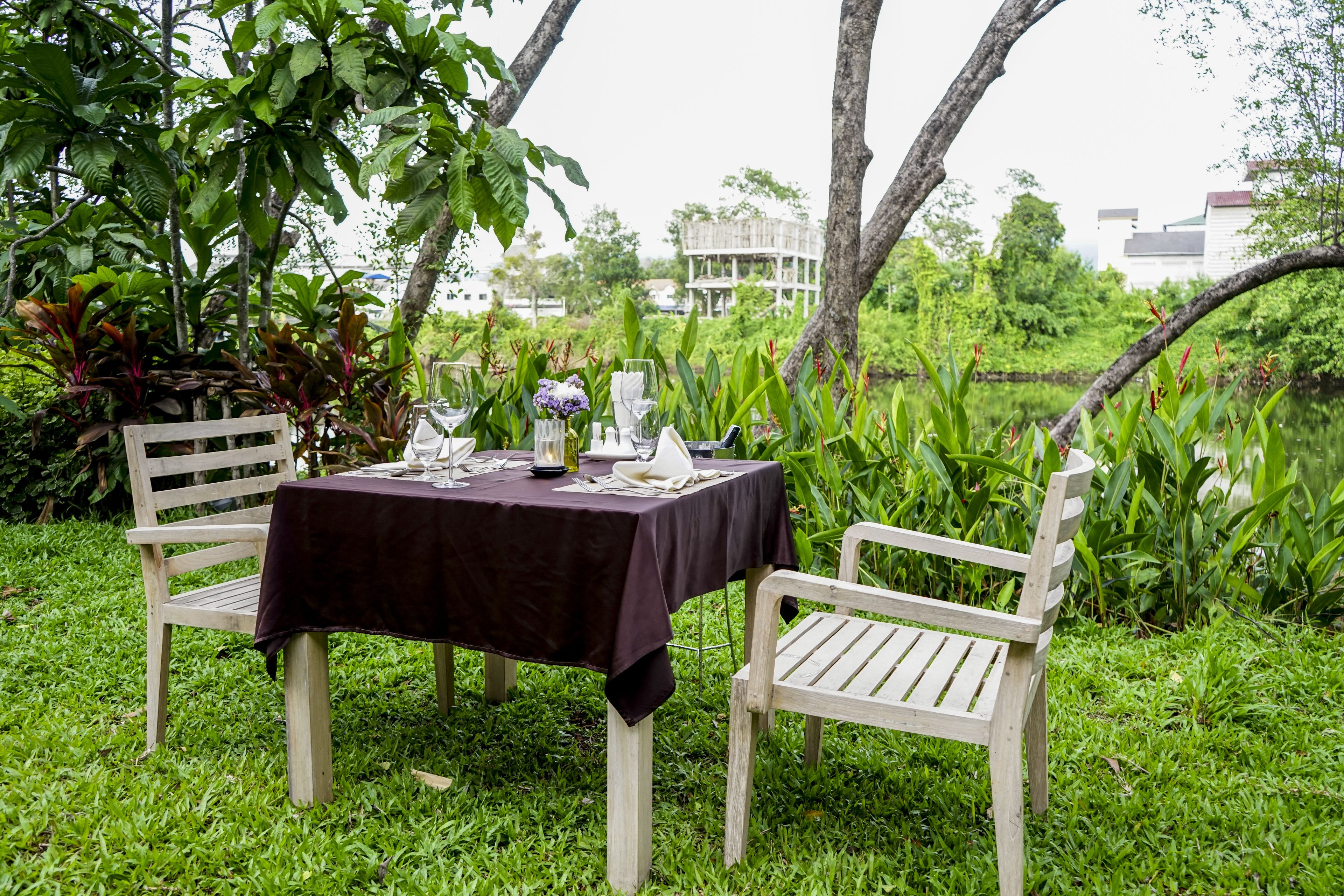 An outdoor dining area with a table set for two, surrounded by lush greenery and trees.