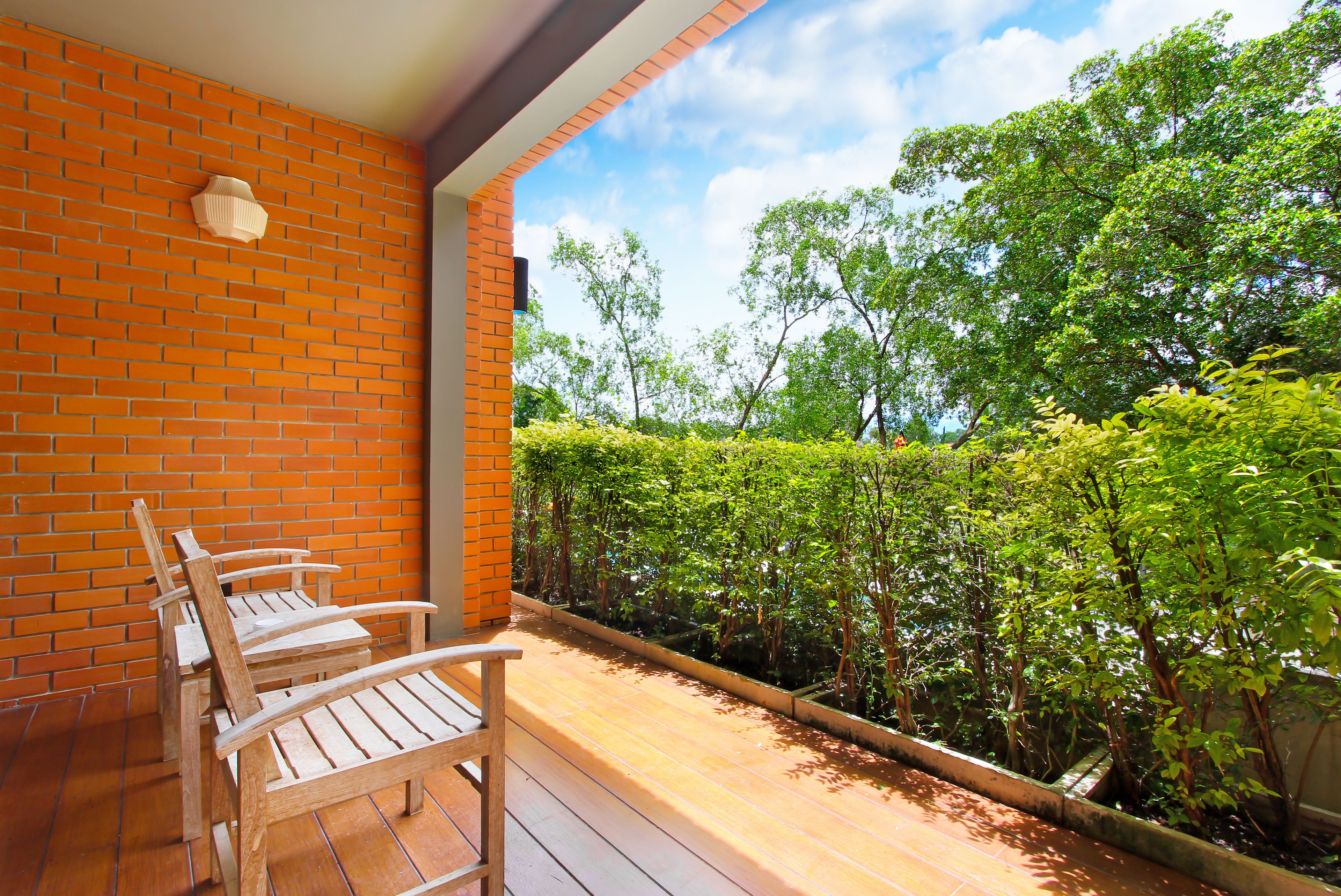 A wooden deck with a brick wall and a view of a lush garden.