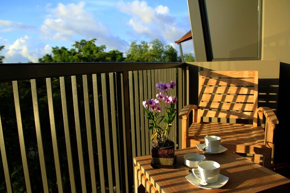 Un balcon avec une table en bois, des chaises et une orchidée en pot.