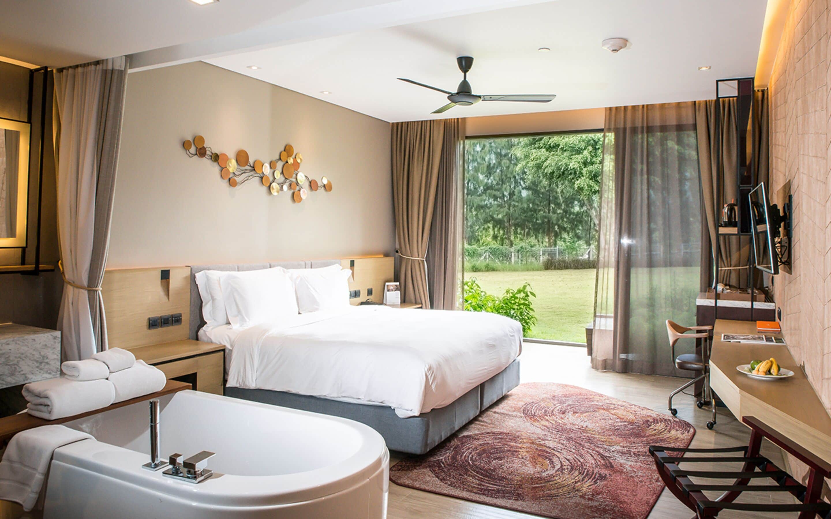 Een moderne hotelkamer met een groot bed, een aparte badkamer met bad, een bureau met stoel en uitzicht op het omliggende landschap.