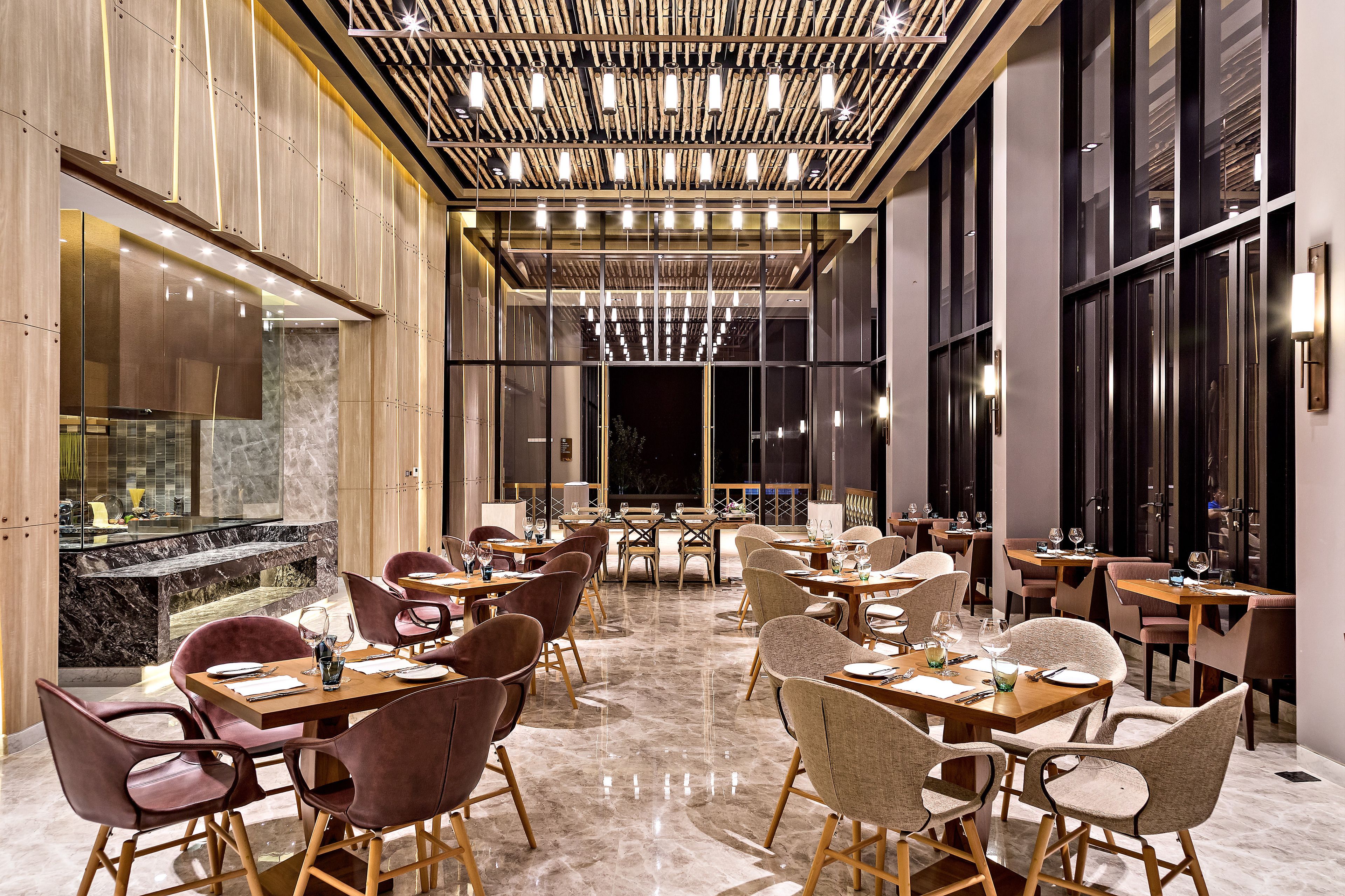 Un espace de restauration moderne, doté de plusieurs tables et chaises, d’un sol en marbre et d’un plafond orné de luminaires suspendus.