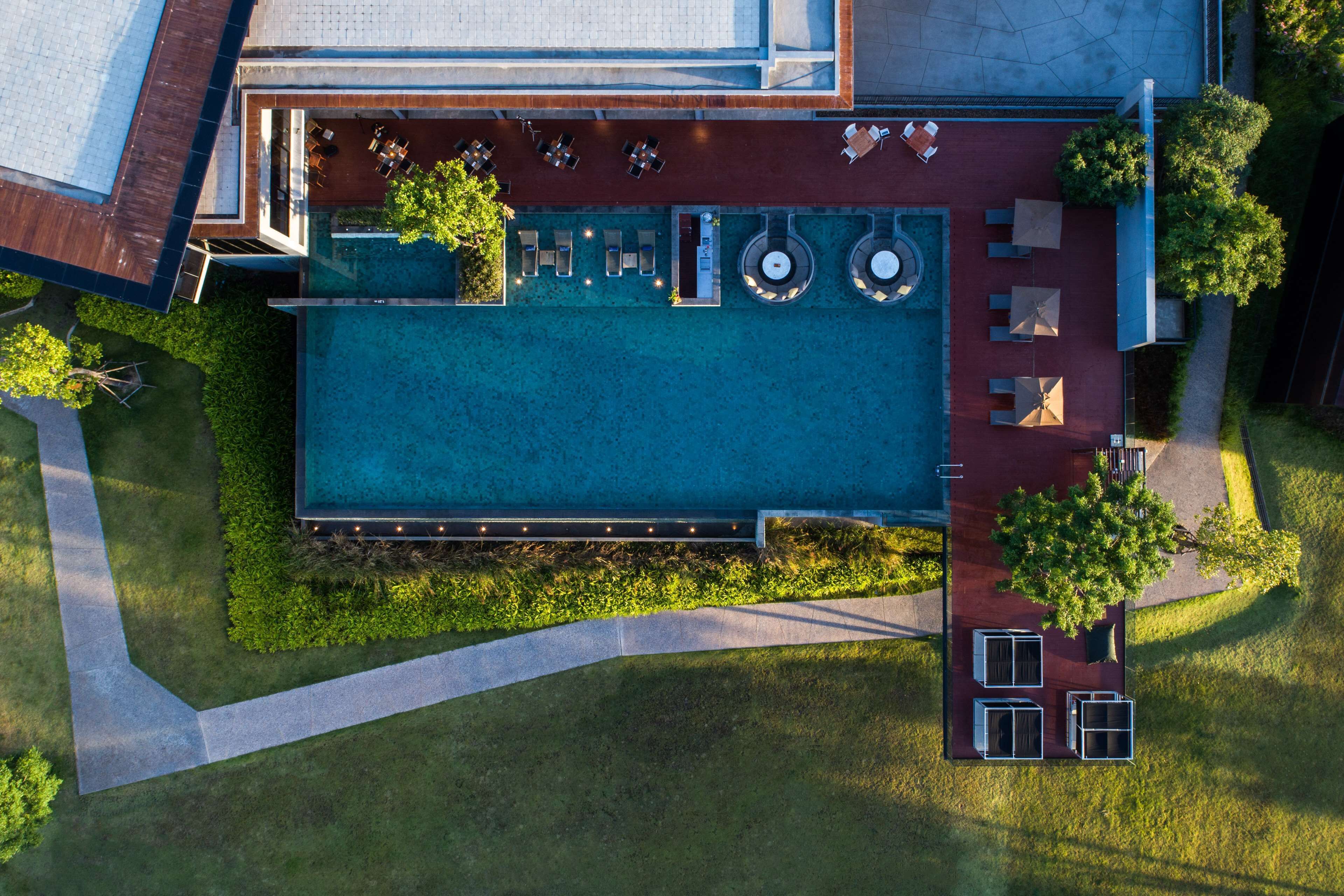 An aerial view of a modern hotel with a swimming pool, outdoor seating, and a landscaped garden.