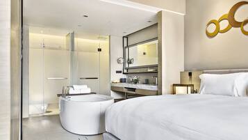 Una habitación de hotel moderna con una cama grande, una bañera redonda, un vestuario de ducha y un tocador con espejo.