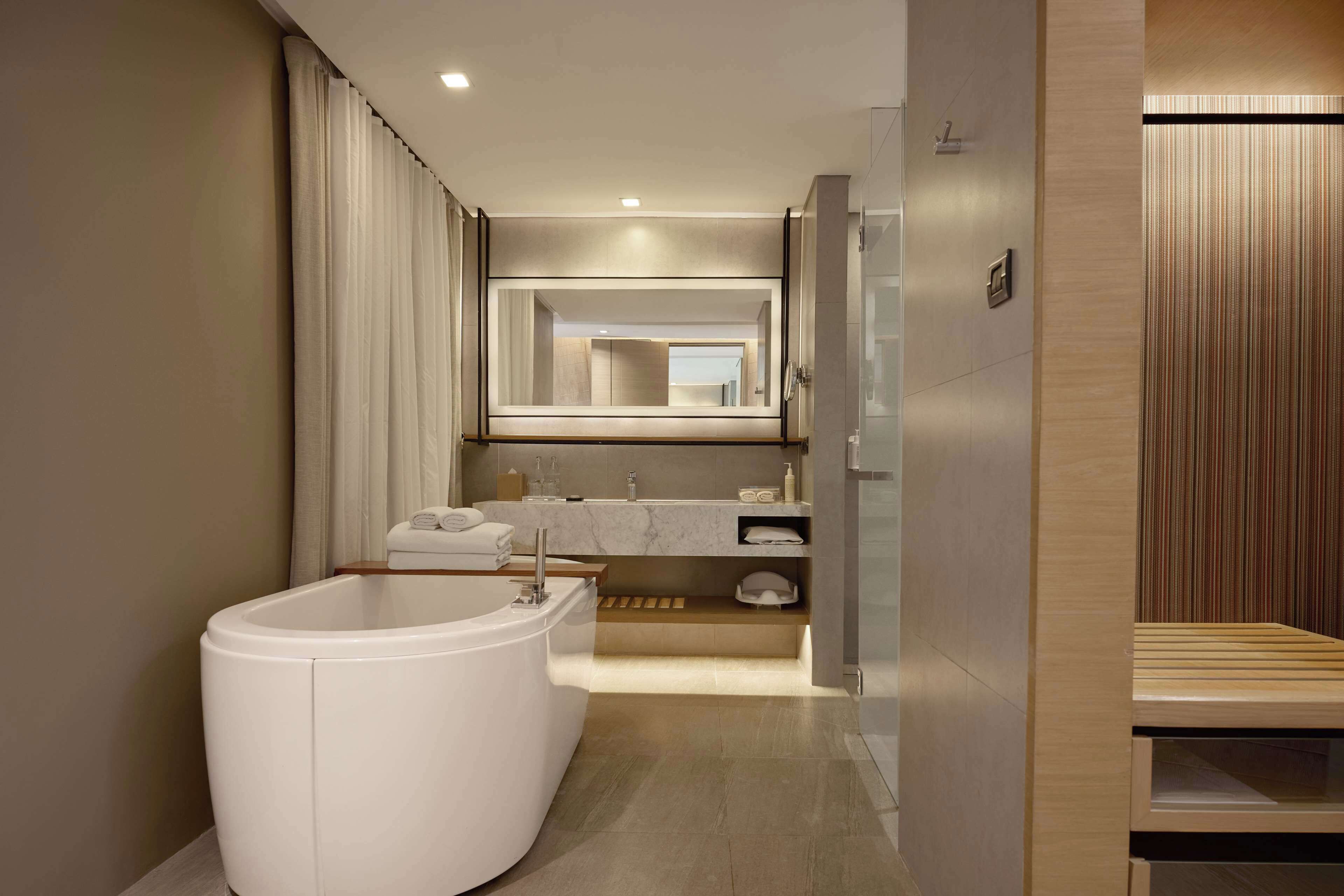 Un baño moderno con una bañera independiente, un espejo grande y un tocador de madera.