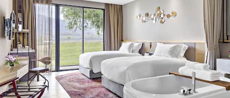 Una habitación de hotel moderna con dos camas, un ventanal con vistas a un paisaje verde, un ventilador de techo y una bañera.