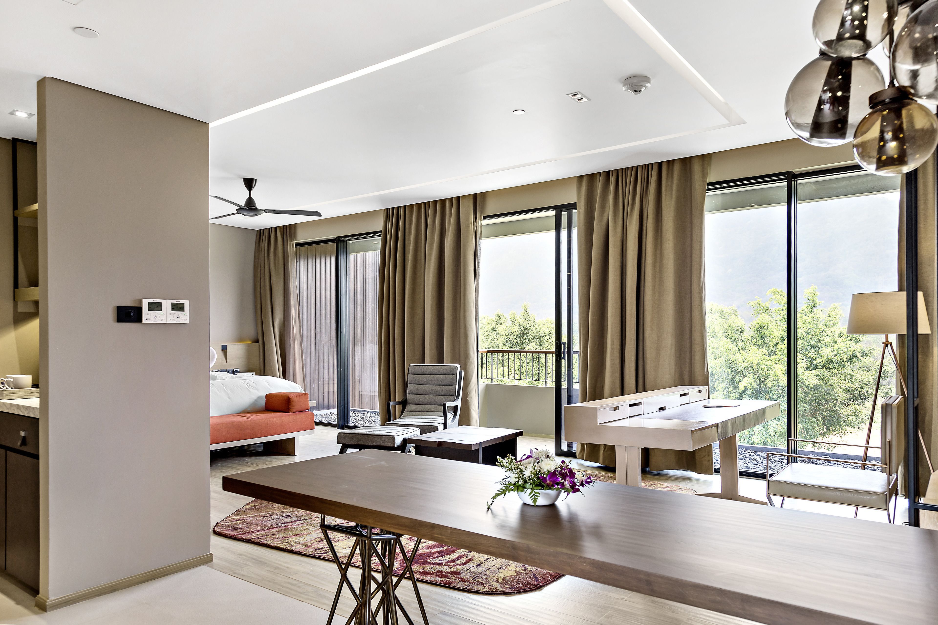 A modern hotel room with a large bed, a dining table, and a balcony with a view.