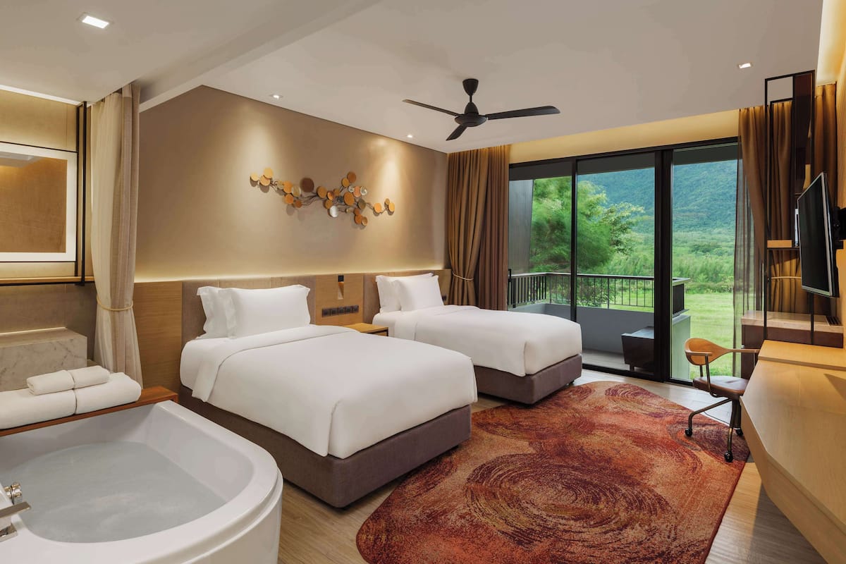 A hotel room with two beds, a large window with a view, a ceiling fan, and a bathtub.