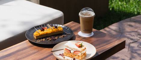 A wooden table with a dessert plate, a cup of coffee, and a slice of cake.