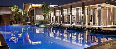 A modern hotel with a large outdoor pool, lounge chairs, and a well-lit reception area.