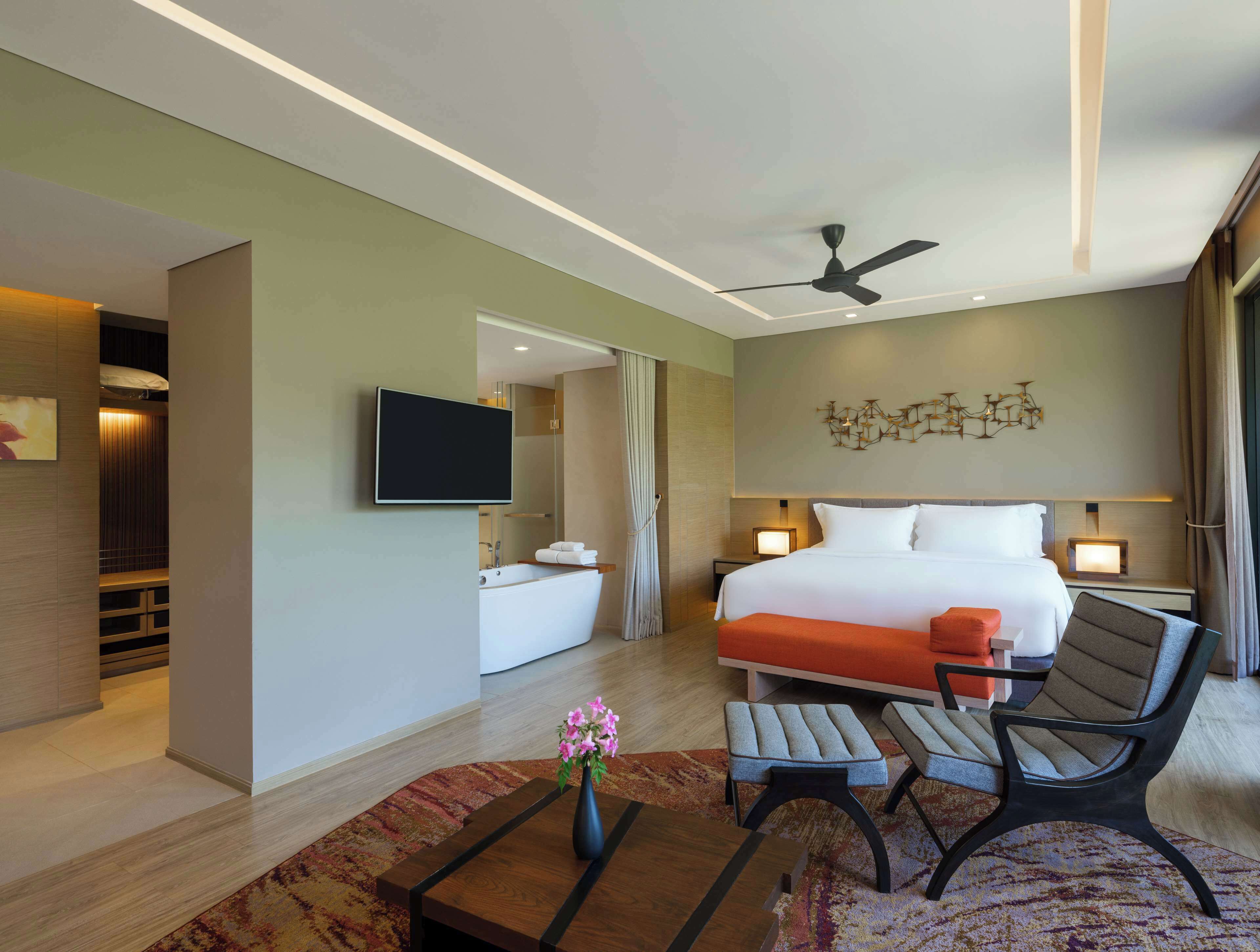 Een moderne hotelkamer met een groot bed, een flatscreen televisie, een plafondventilator, een badkamer met bad en een zithoek met twee stoelen en een tafel.
