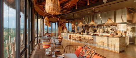 Un comedor amplio con techo alto, ventanas grandes que ofrecen vistas al paisaje y una zona de bar con electrodomésticos de cocina a la vista.