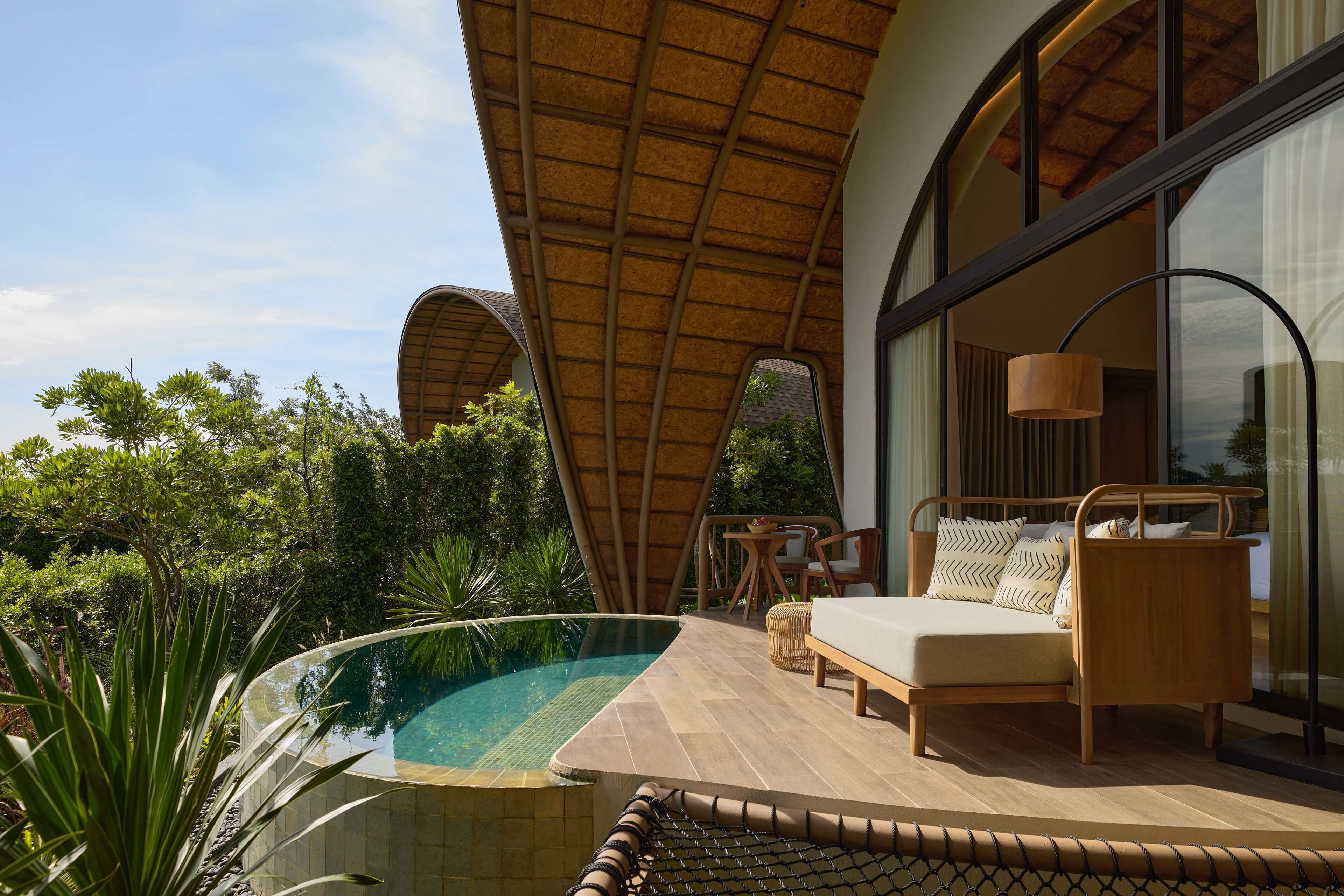 Un espacio lounge moderno al aire libre con piscina, mobiliario de madera y grandes ventanales con vistas a un jardín exuberante.