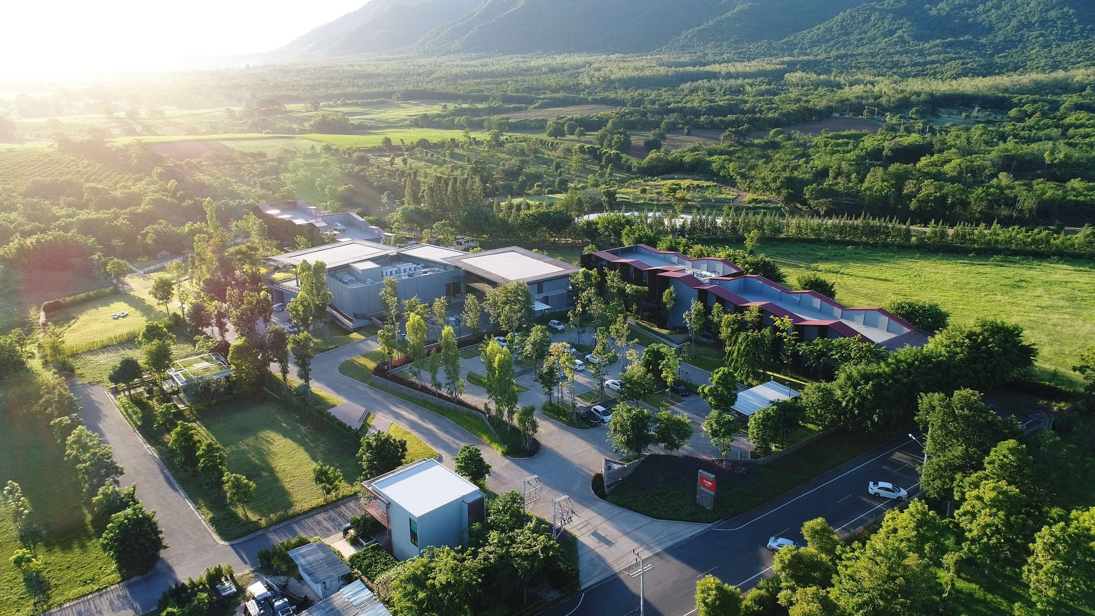 An aerial view of a modern building complex with multiple structures, surrounded by lush greenery and a hilly landscape.