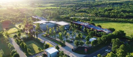 An aerial view of a modern building complex with multiple structures, surrounded by lush greenery and a hilly landscape.