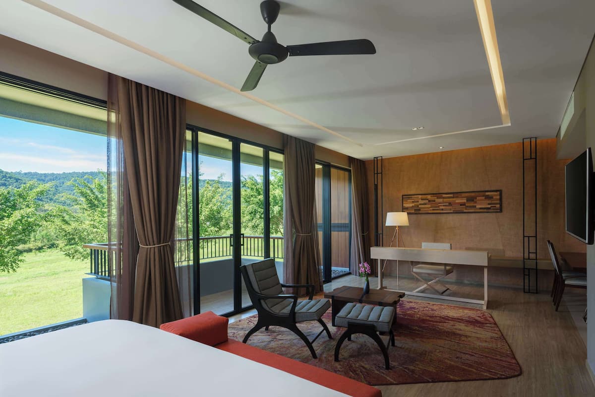 A hotel room with a large bed, a desk with a chair, a ceiling fan, and a view of the outdoors.