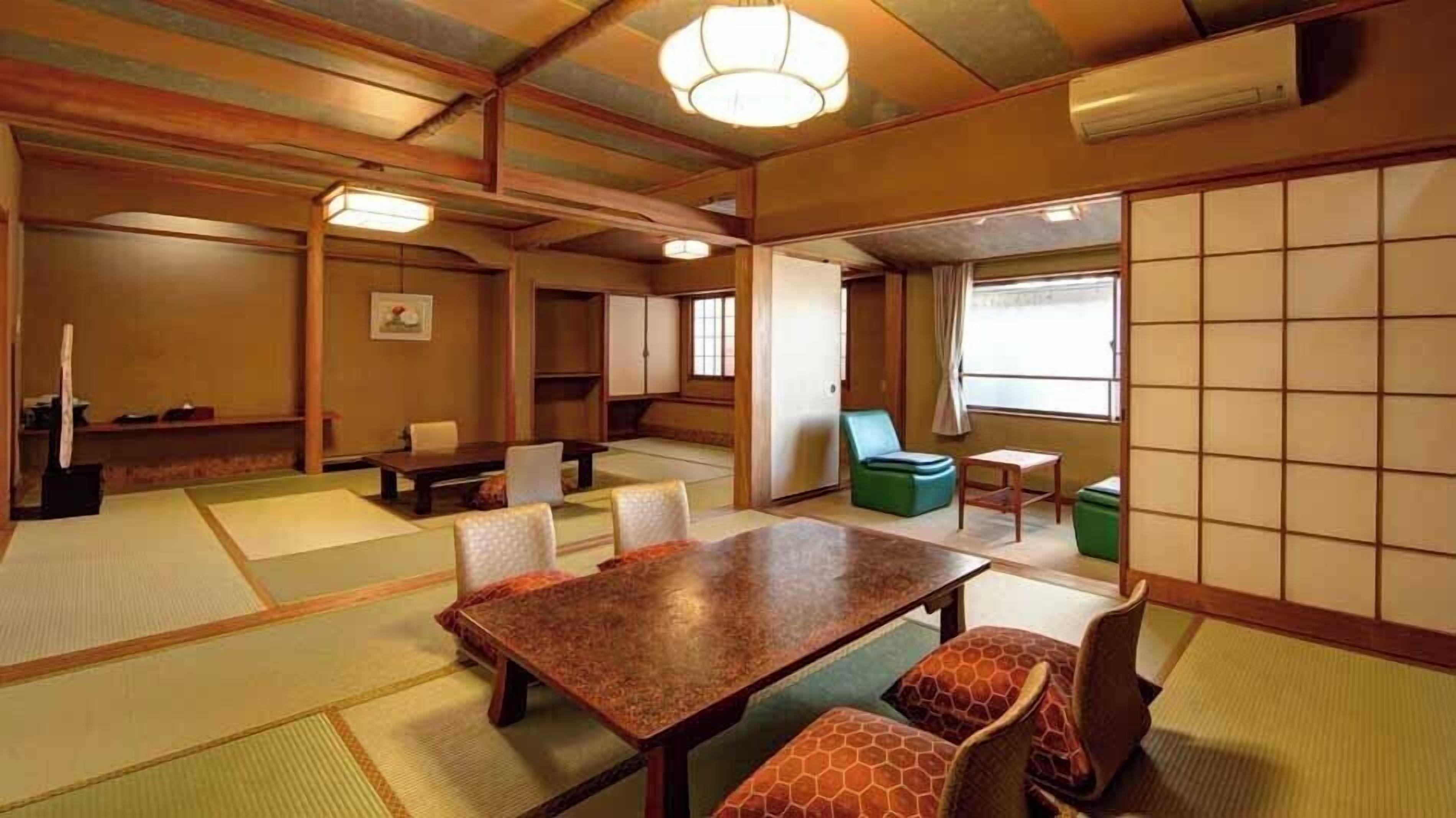 A traditional tatami mat room with a wooden table and chairs, a green sofa, and a sliding door.
