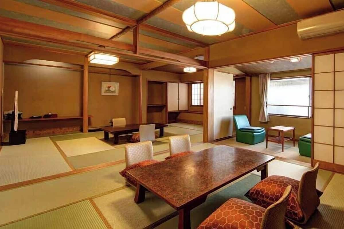 Um quarto tradicional com esteiras de tatame, uma mesa de madeira e cadeiras, um sofá verde e uma porta deslizante.