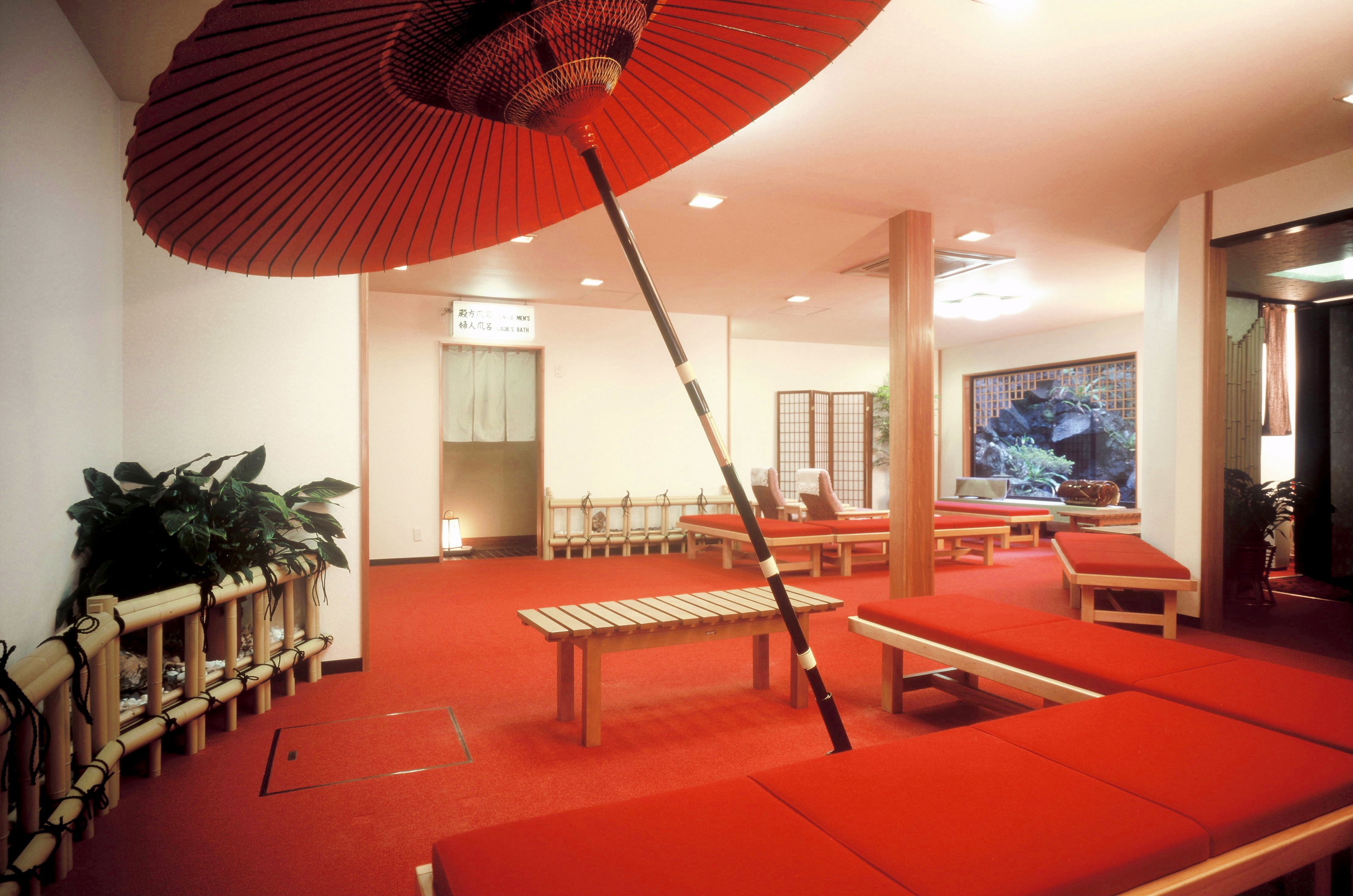 A room with red cushioned seating, a wooden bench, and a red umbrella.