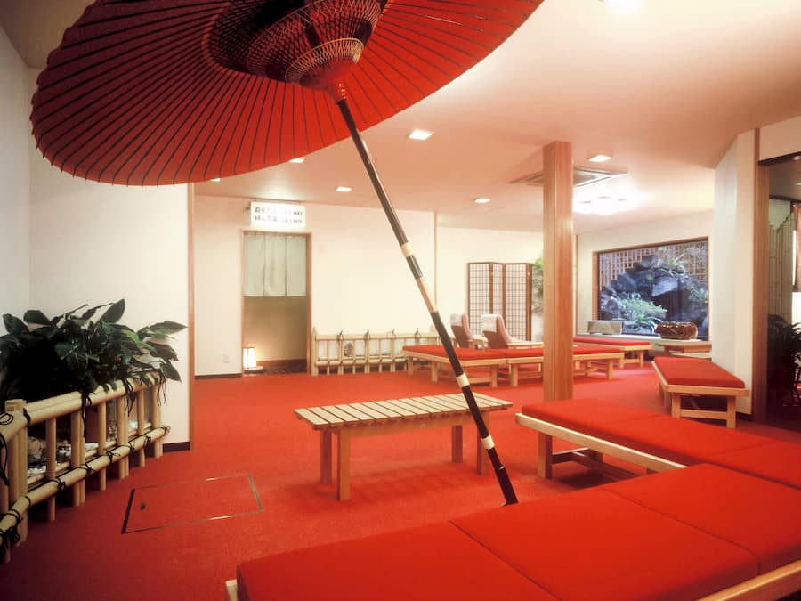 A room with red cushioned seating, a wooden bench, and a red umbrella.