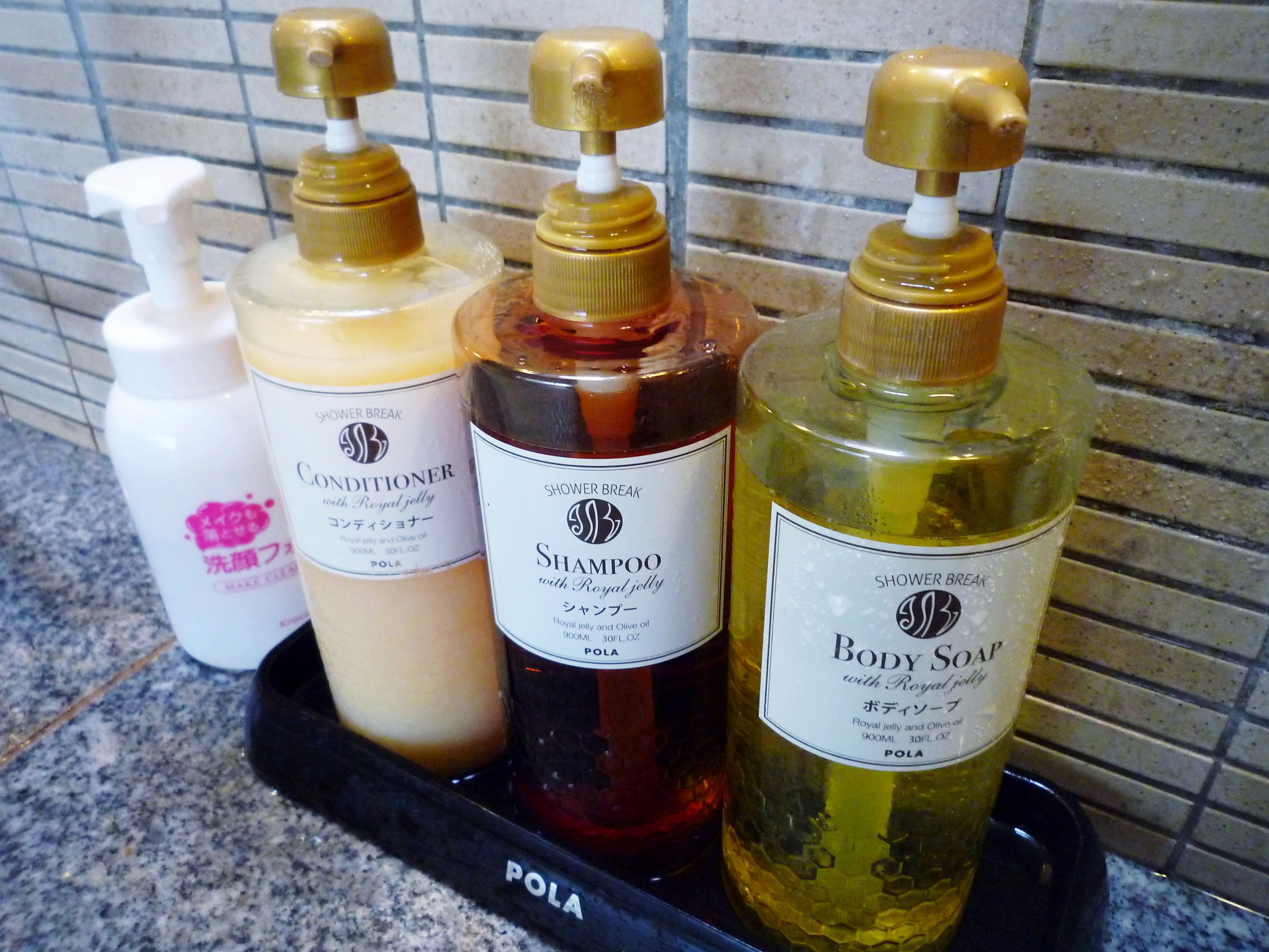 A set of four bottles of shower products on a black tray.
