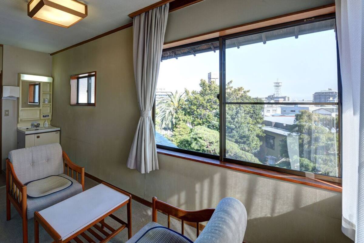 A room with a large window, a wooden chair, a small table, a mirror, and a door.