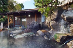 A traditional Japanese building with a wooden exterior and a stone waterfall feature. - Ito Onsen Yokikan (Ito)