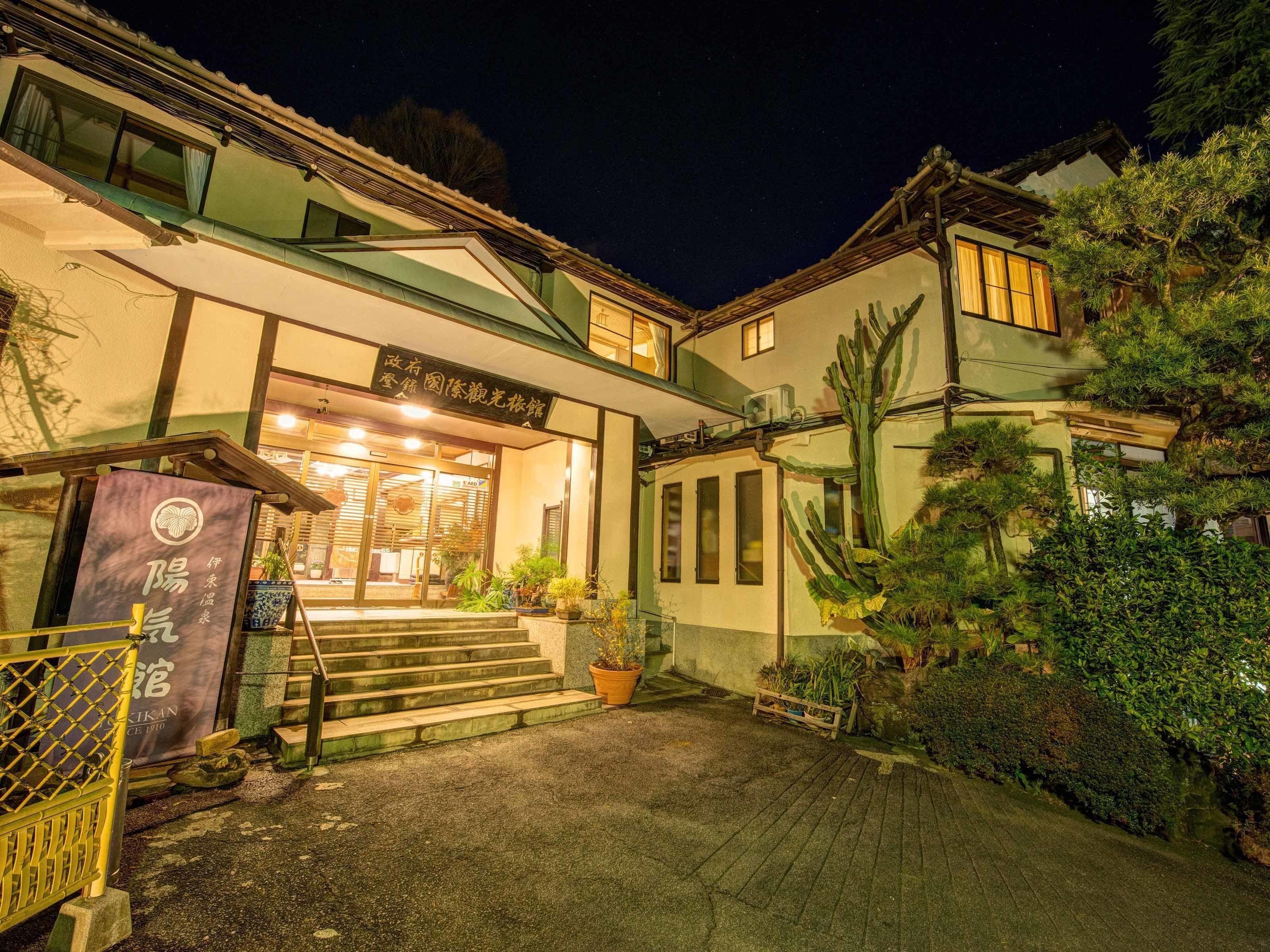 Un edificio tradicional japonés con una entrada bien iluminada, escalones que conducen a la puerta y una variedad de plantas en macetas y cactus alrededor del exterior.