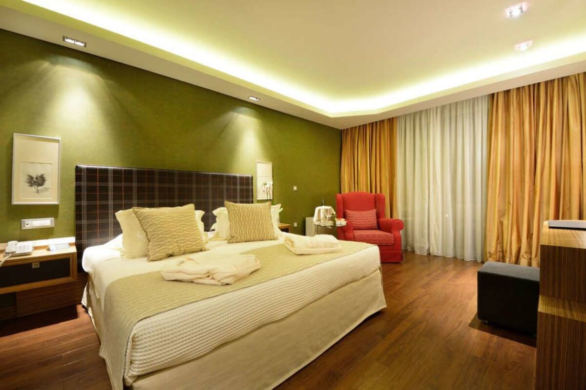 A hotel room with a large bed, a red armchair, a desk, and a view of the curtains.