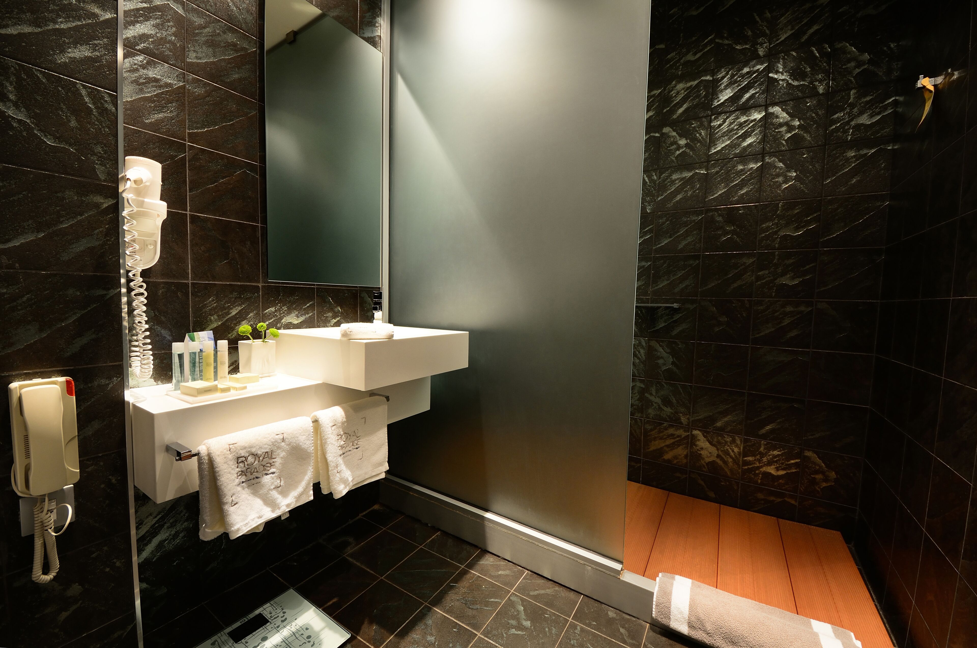 Un baño moderno con pared de mármol, un lavamanos blanco, un espejo y zona de ducha.