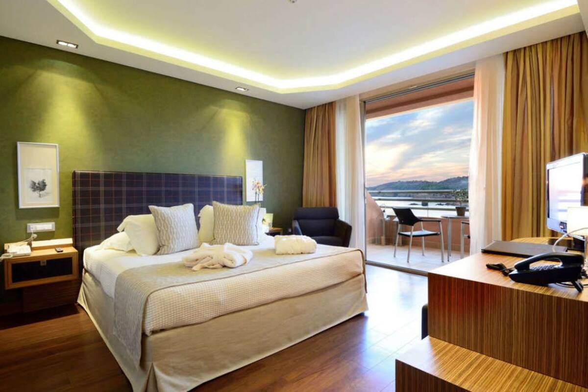 A hotel room with a large bed, a desk with a phone, and a view of the outdoors.