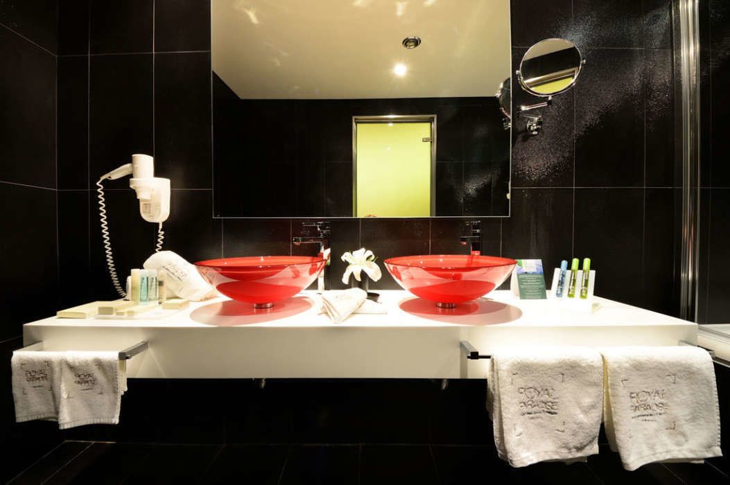 A modern bathroom with a large mirror, two red sinks, a hairdryer, and toiletries on the counter.
