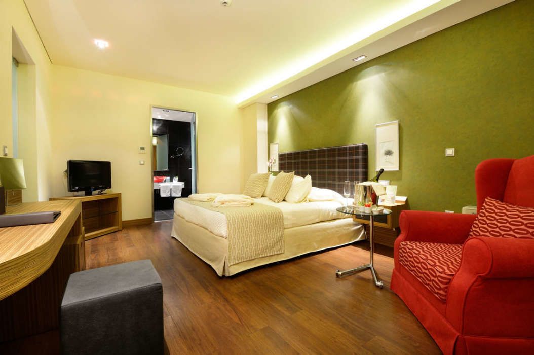A modern hotel room with a bed, a desk, a red armchair, and a television.