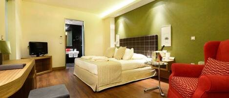 A modern hotel room with a bed, a desk, a red armchair, and a television.