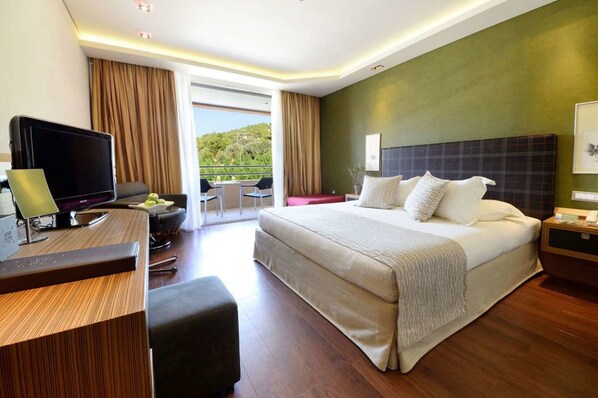 A modern hotel room with a large bed, a desk with a computer, a TV, and a balcony with a scenic view. - Royal Paradise Beach Resort & Spa (Thasos)
