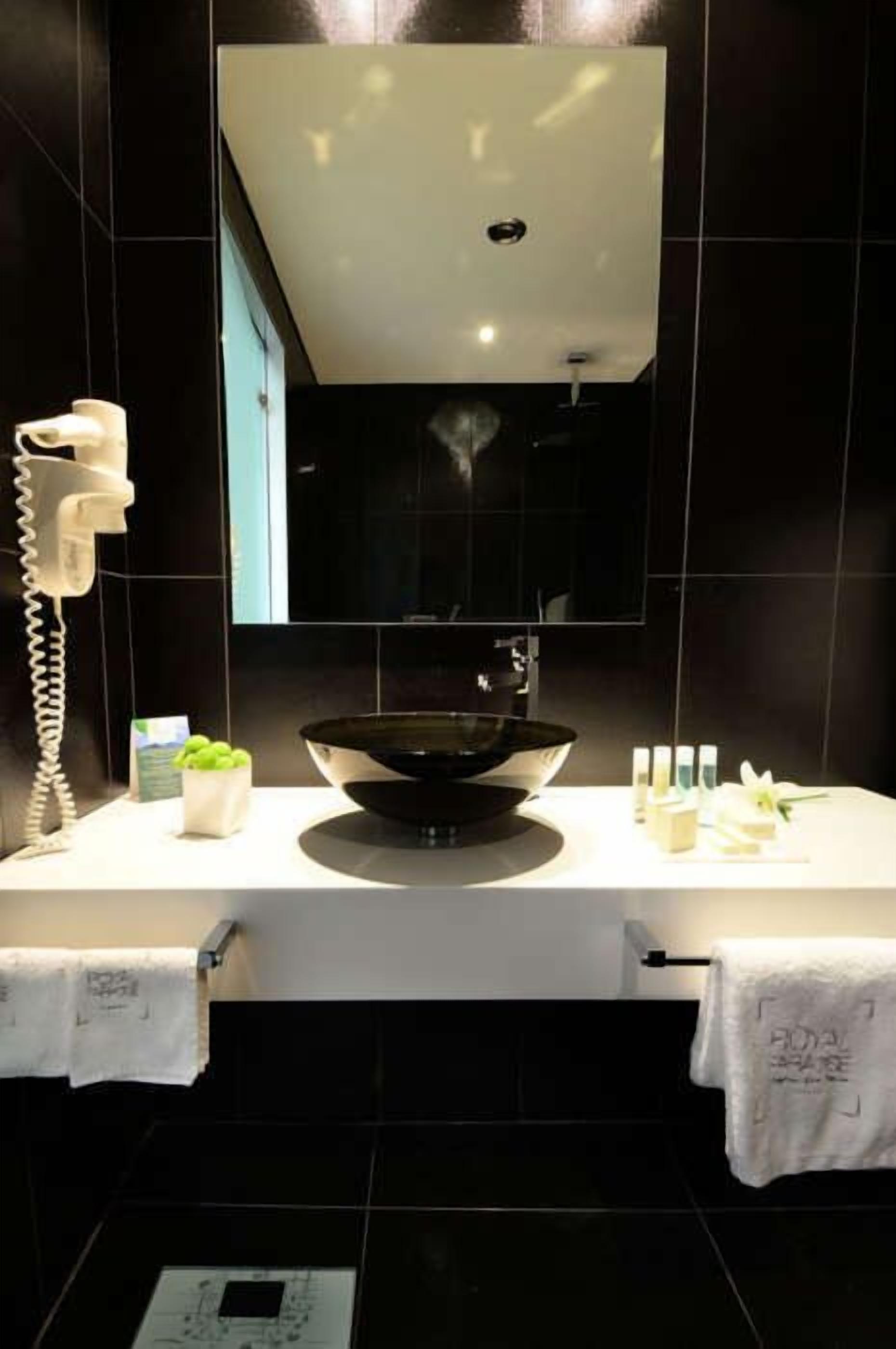 Un baño moderno con un lavabo negro, un espejo encima y un perchero para toallas.