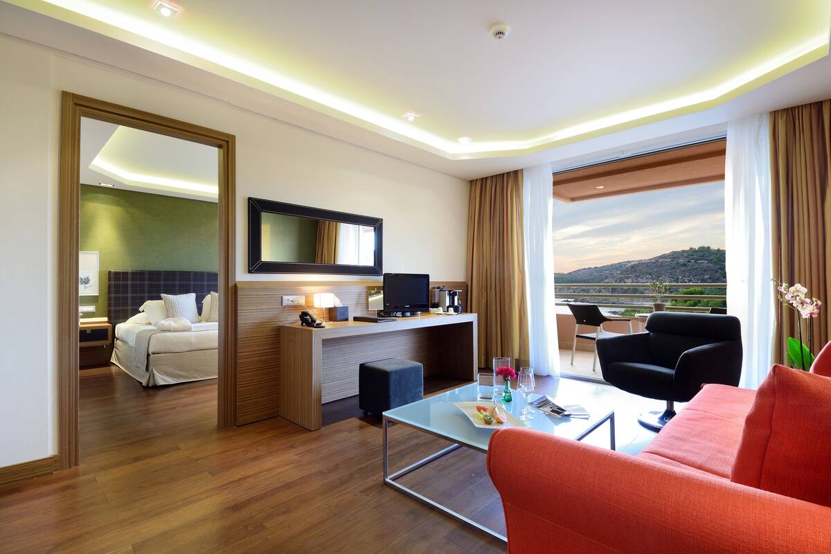 A hotel room with a bed, desk, TV, and a balcony with a view.