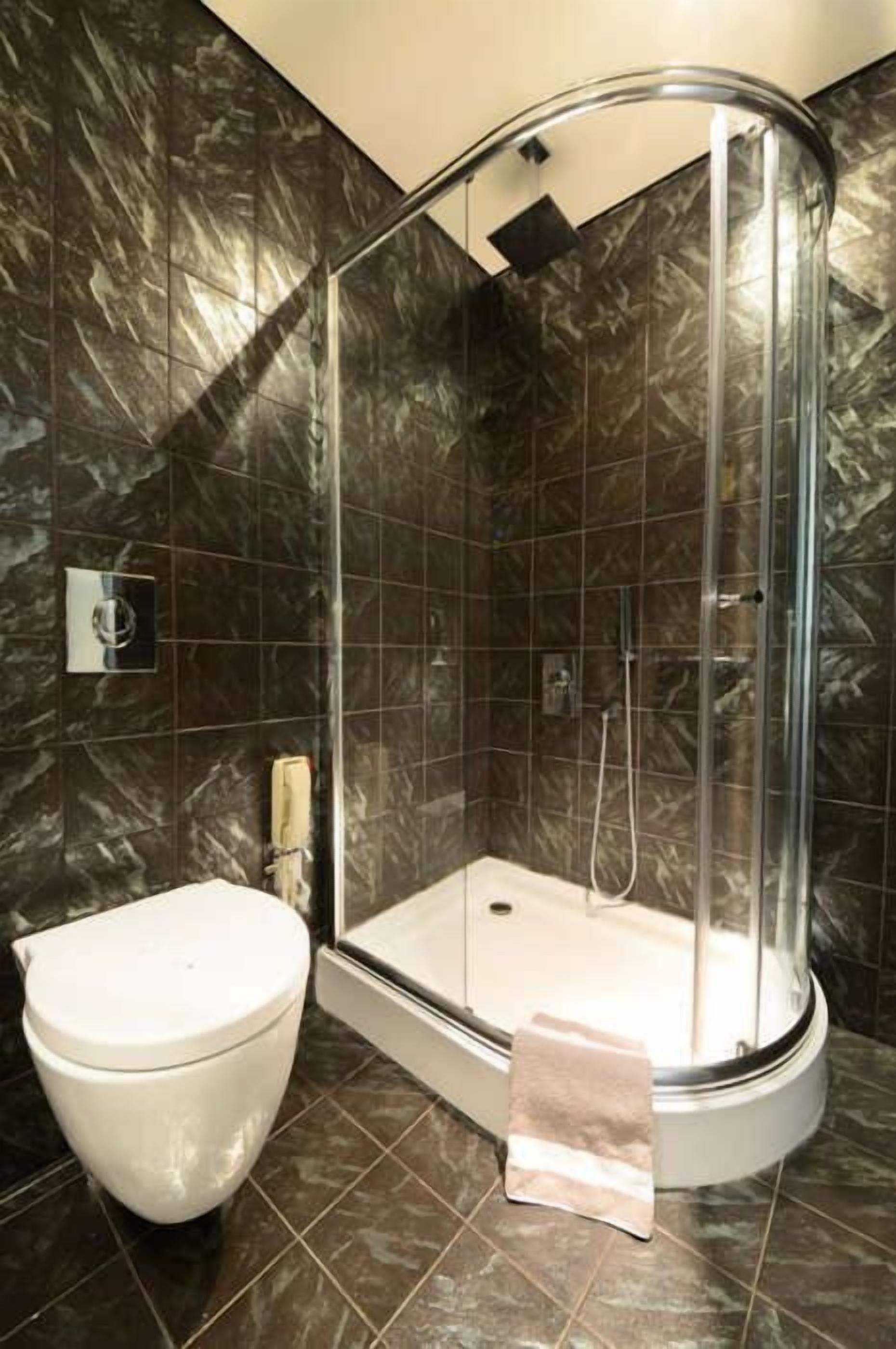 Un bagno moderno con doccia vetrata, un WC bianco e piastrelle di marmo scuro.