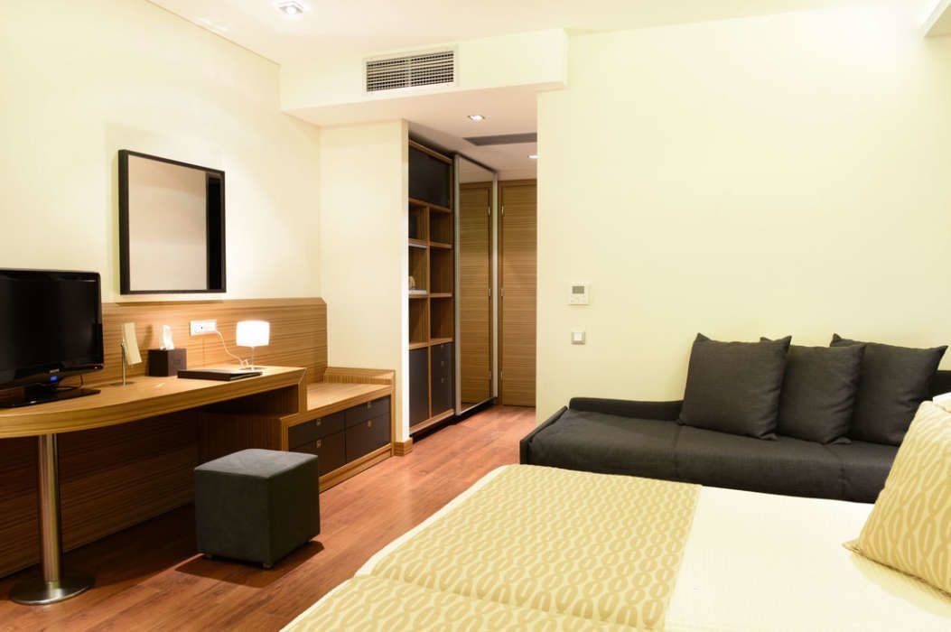 Habitación de hotel con cama, escritorio con computadora, televisor, armario y sofá.