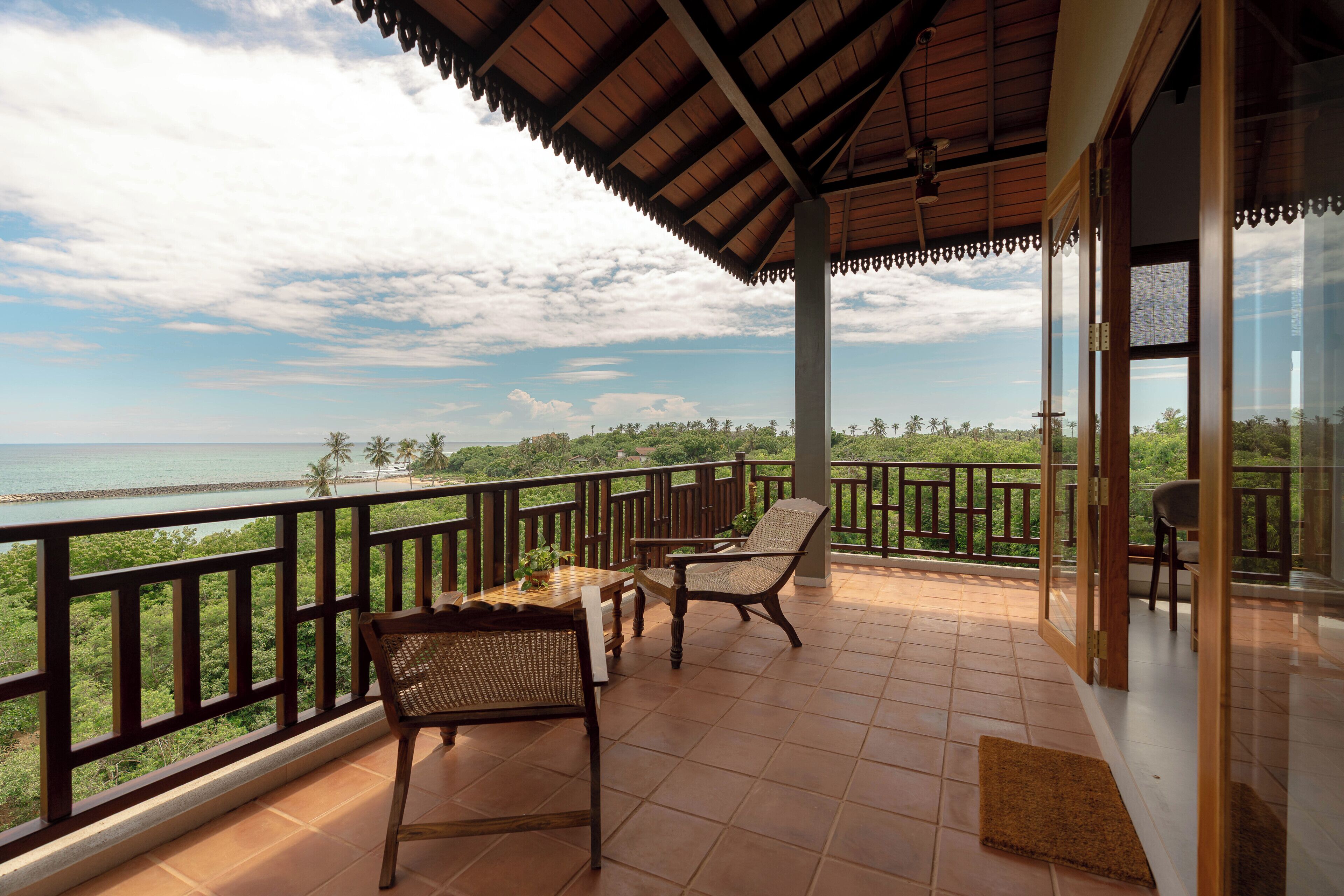 A balcony with a view of the sea, wooden furniture, and a tiled floor.