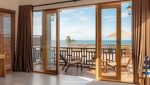 Una habitación con un gran ventanal corredero que da a un balcón con vista al mar.