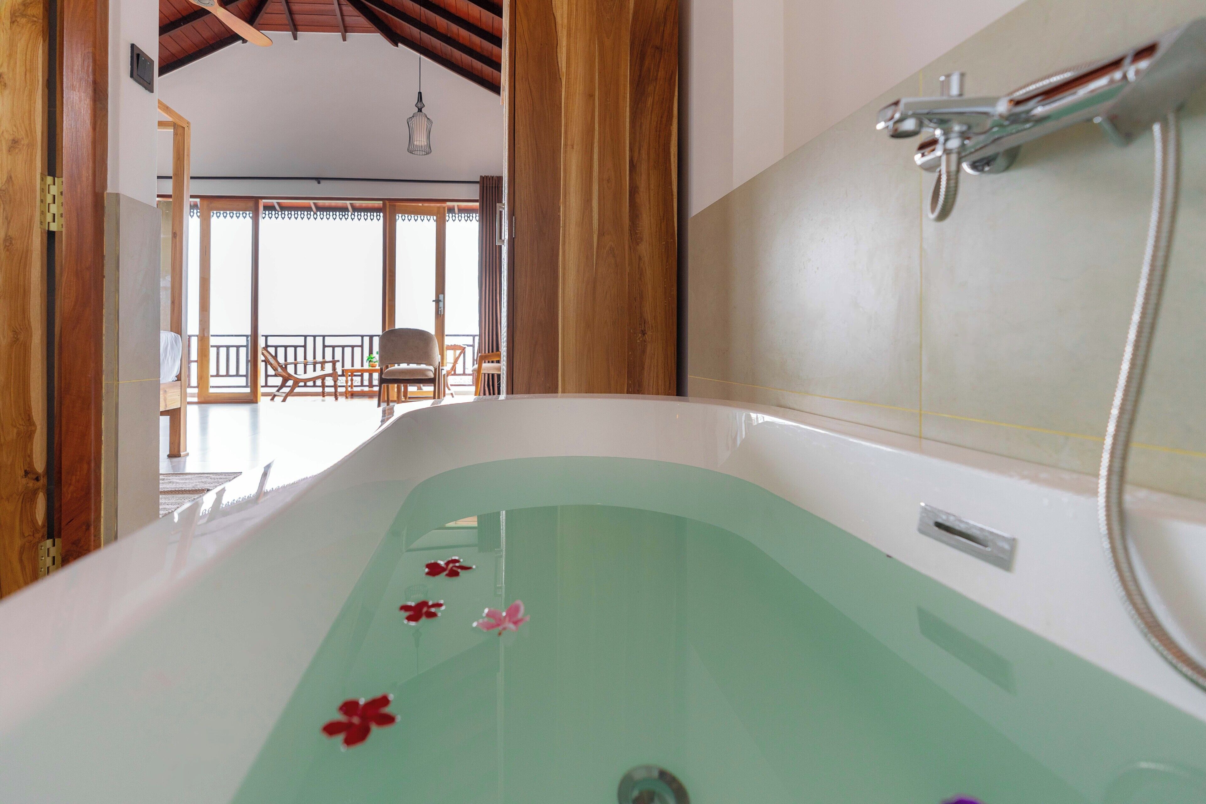 A bathtub with a showerhead, a wooden door, and a view of a balcony with chairs.