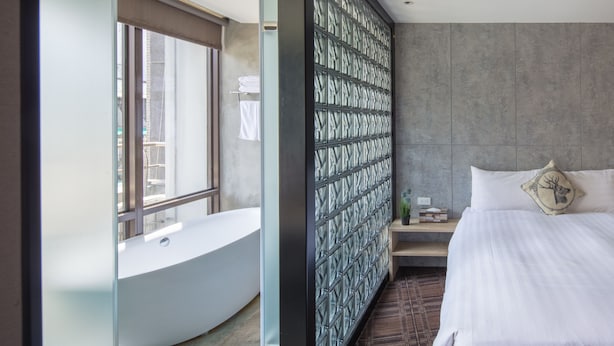A modern hotel room with a large bathtub, a bed with white linens, and a decorative wall panel. - Roaders Hotel Zhonghua (Taipei)