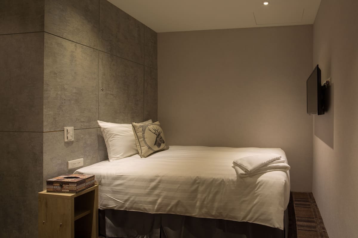 A modern bedroom with a large bed, a wooden nightstand, and a flat-screen TV mounted on the wall.