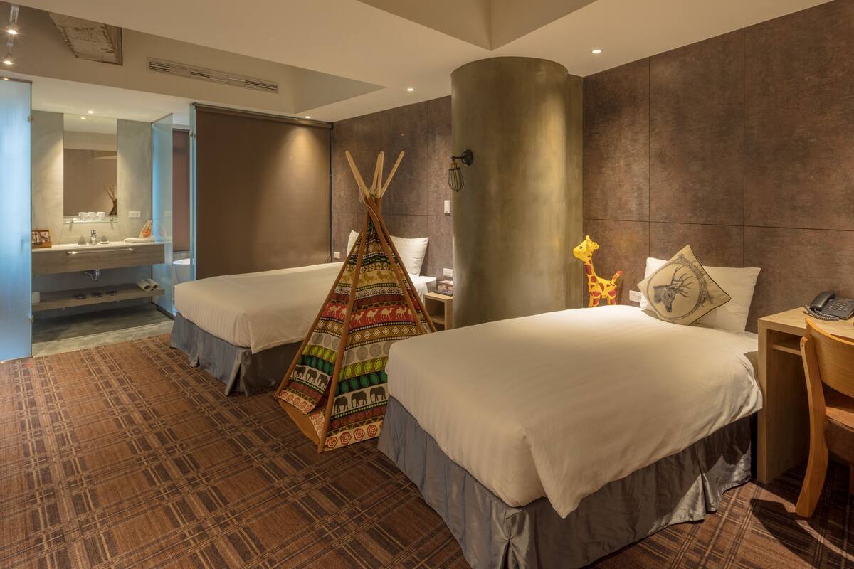 A hotel room with two beds, a large mirror, a bathroom with a sink, and a unique teepee decoration.