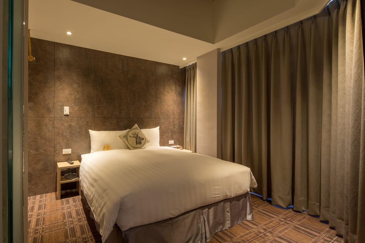 A modern hotel room with a large bed, a nightstand, and a headboard with a deer motif.
