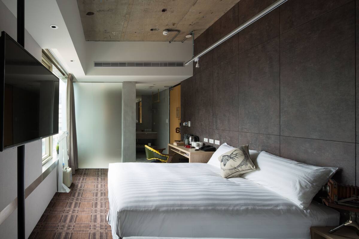 A modern hotel room with a large bed, a flat-screen TV, a desk, and a chair.