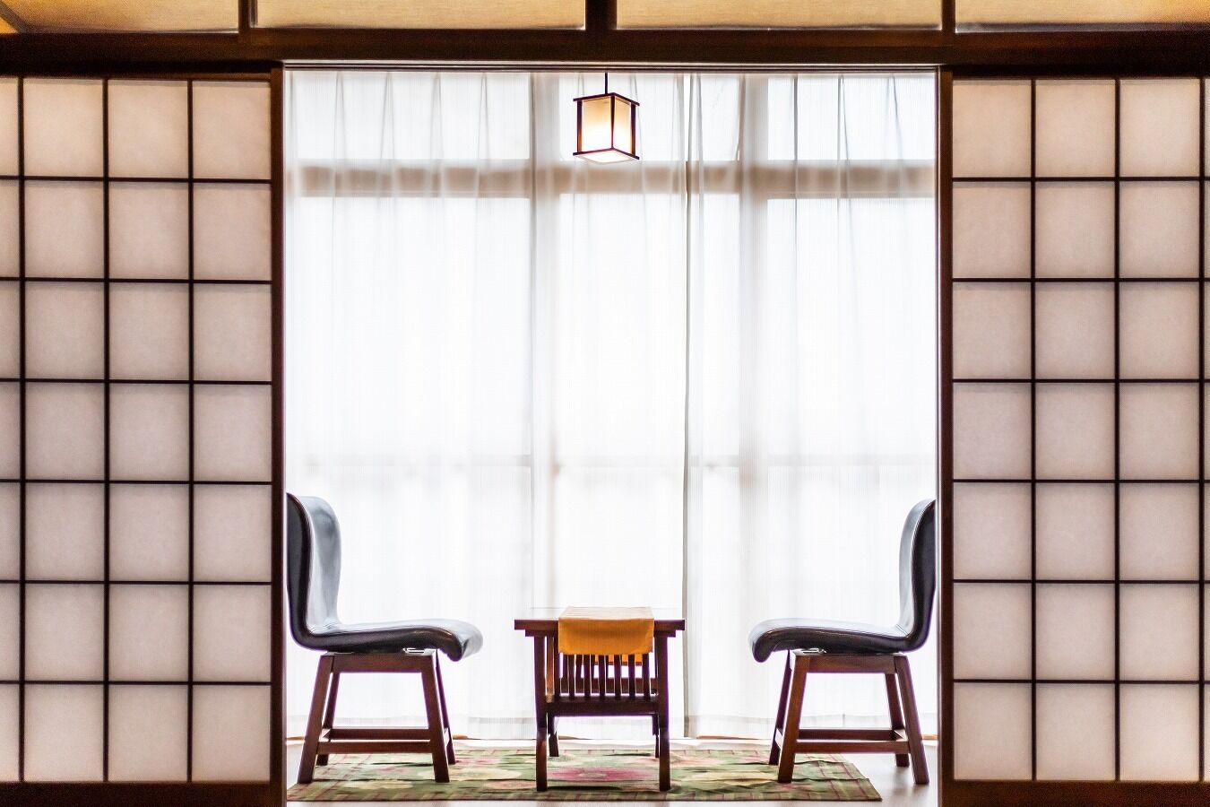 A room with tatami mat flooring, a shoji screen, two chairs, and a small table.
