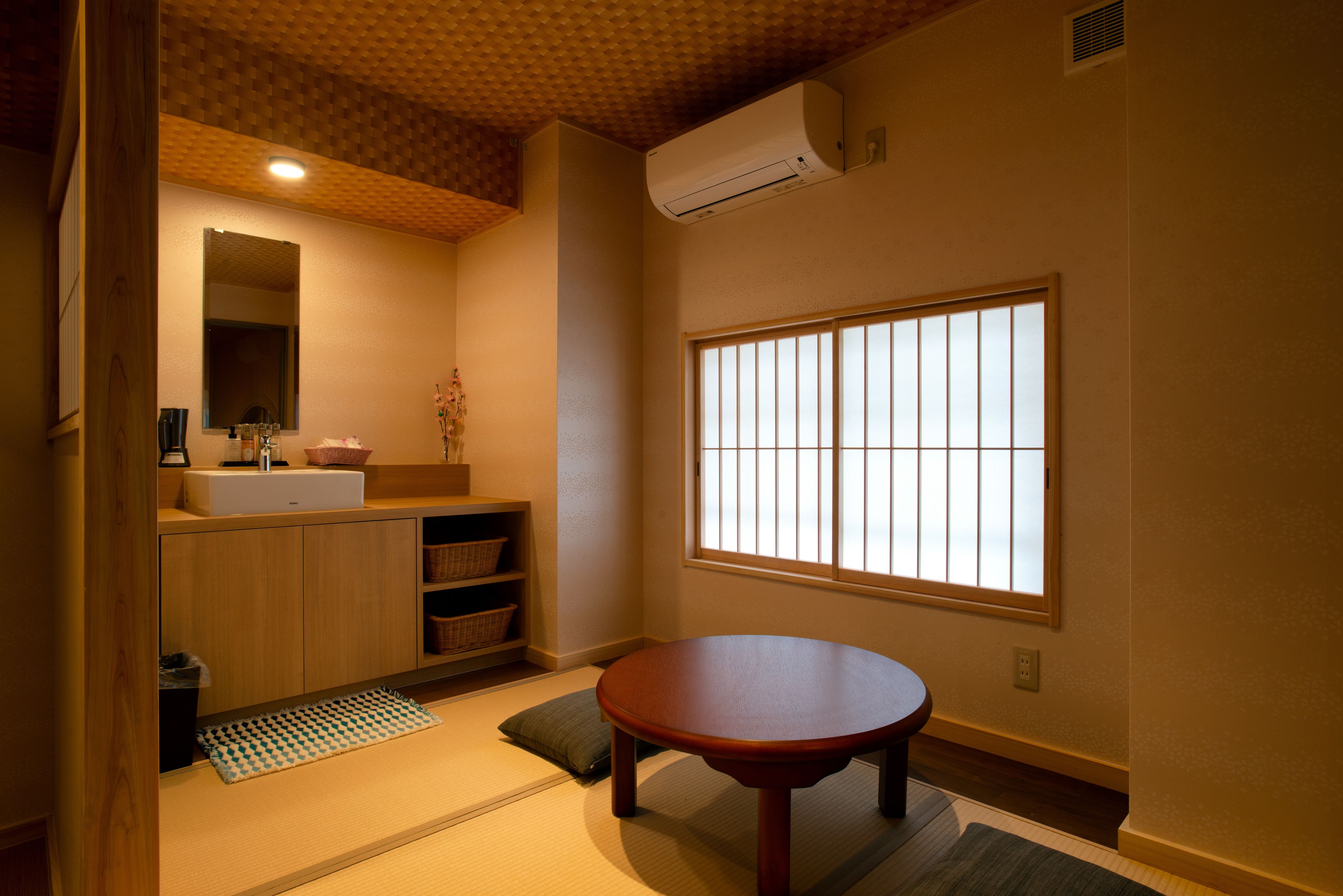 A traditional Japanese-style room with tatami flooring, a wooden table, a built-in shelf, a sink, and a window with shoji screens.