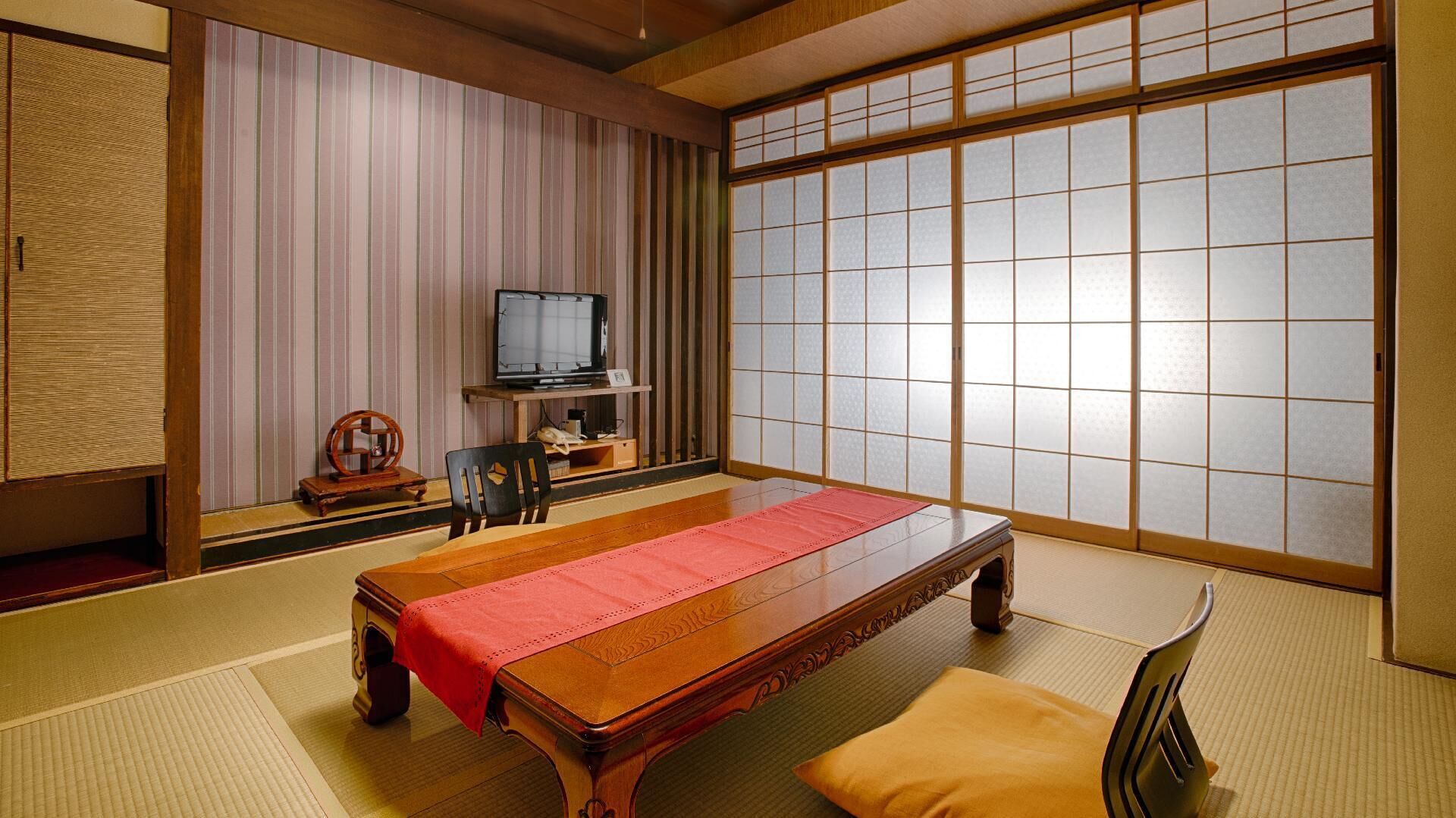A traditional Japanese room with tatami flooring, a low wooden table, a television, and sliding shoji doors.